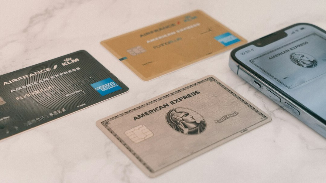 Hand holding a smartphone next to a bank card on a light desk